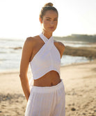 A woman wearing a white linen top and high waist linen pants standing on a beach.