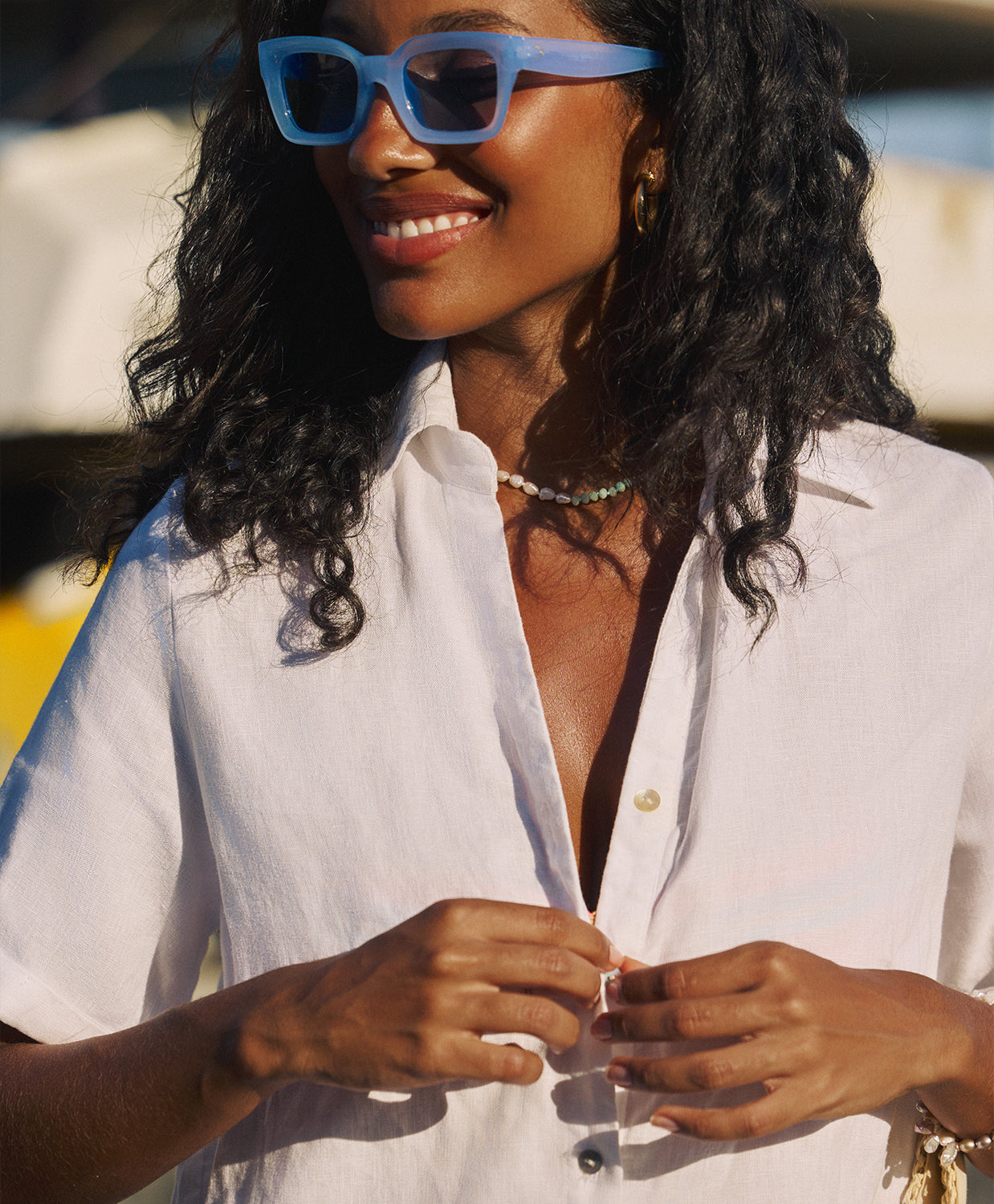 A woman wearing a white button down romper standing outside in the sun. 