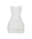 A white mini strapless dress with a ruffle bottom against a white wall.