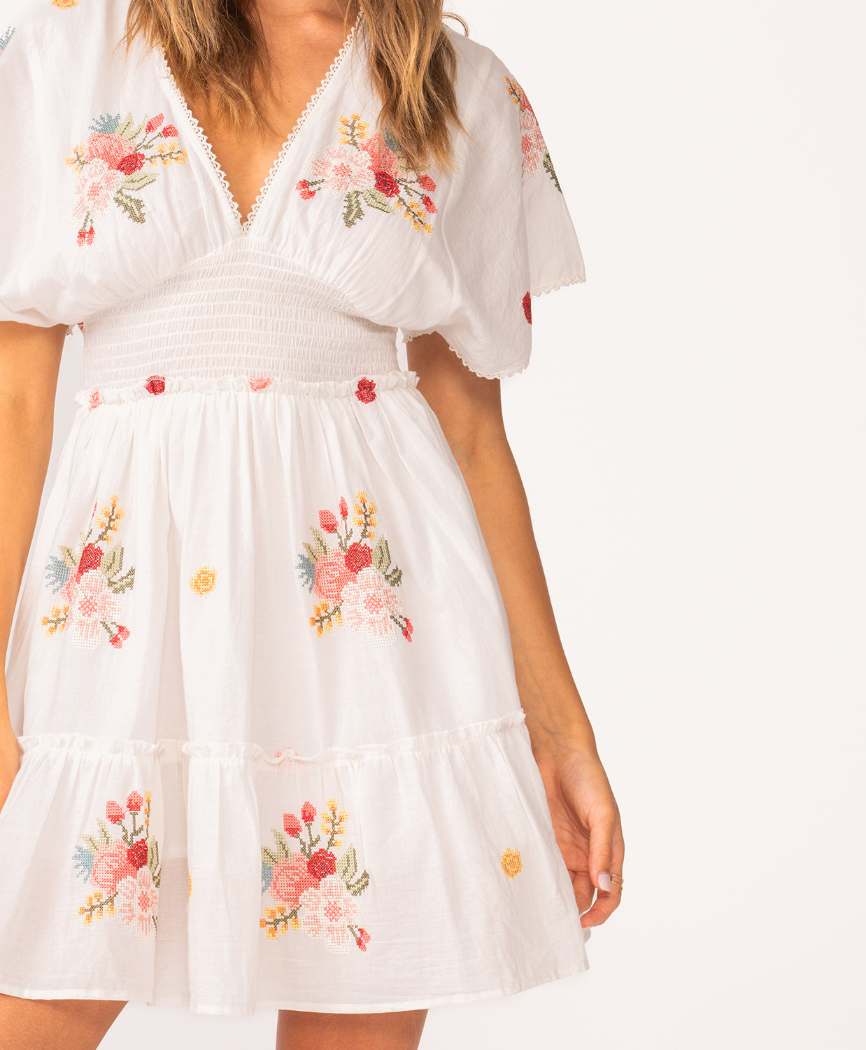 A woman wearing a short sleeve dress with floral details standing against a white wall.