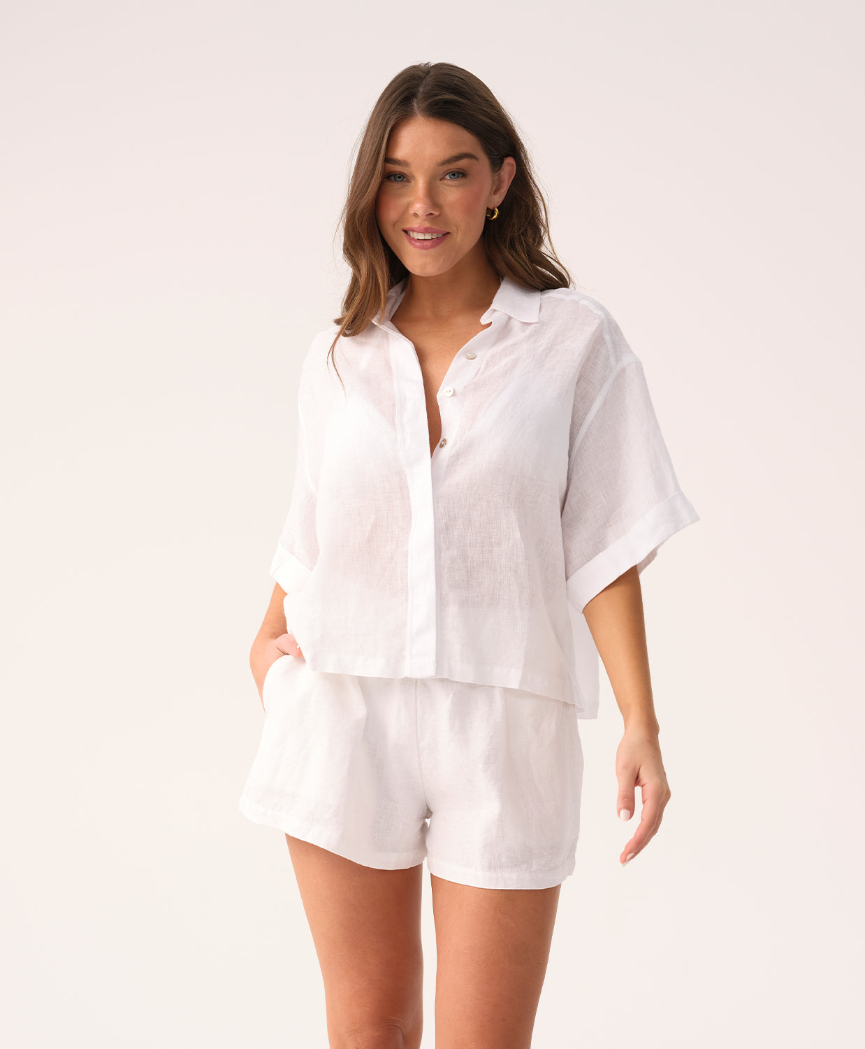 Woman wearing a white short sleeve shirt and short set on a plain background