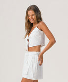 Woman wearing a white lace top and skirt set against a plain background