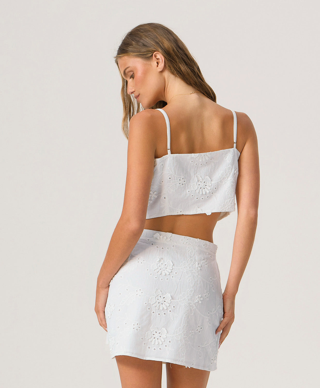 Woman wearing a white embroidered top and skirt set on a white background