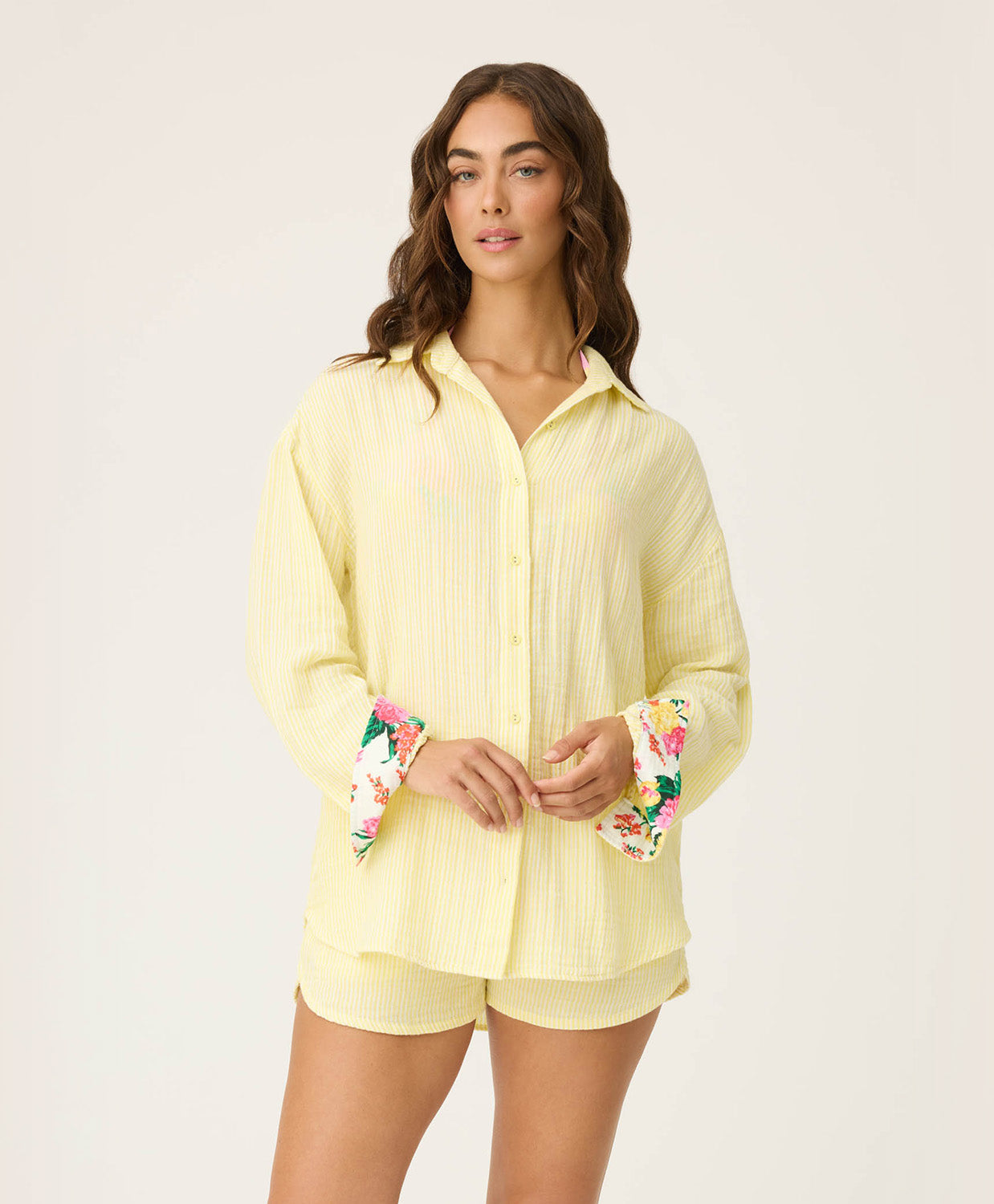 Woman wearing a light yellow shirt with floral cuffs and matching shorts on a white background