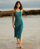 A woman wearing a teal mid length dress walking on the beach. 