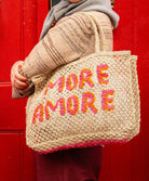 A woman holding a tote/bag that reads "More Amore" in pink and orange. 