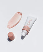 A lip gloss tube, cap, and sample against a white wall. 