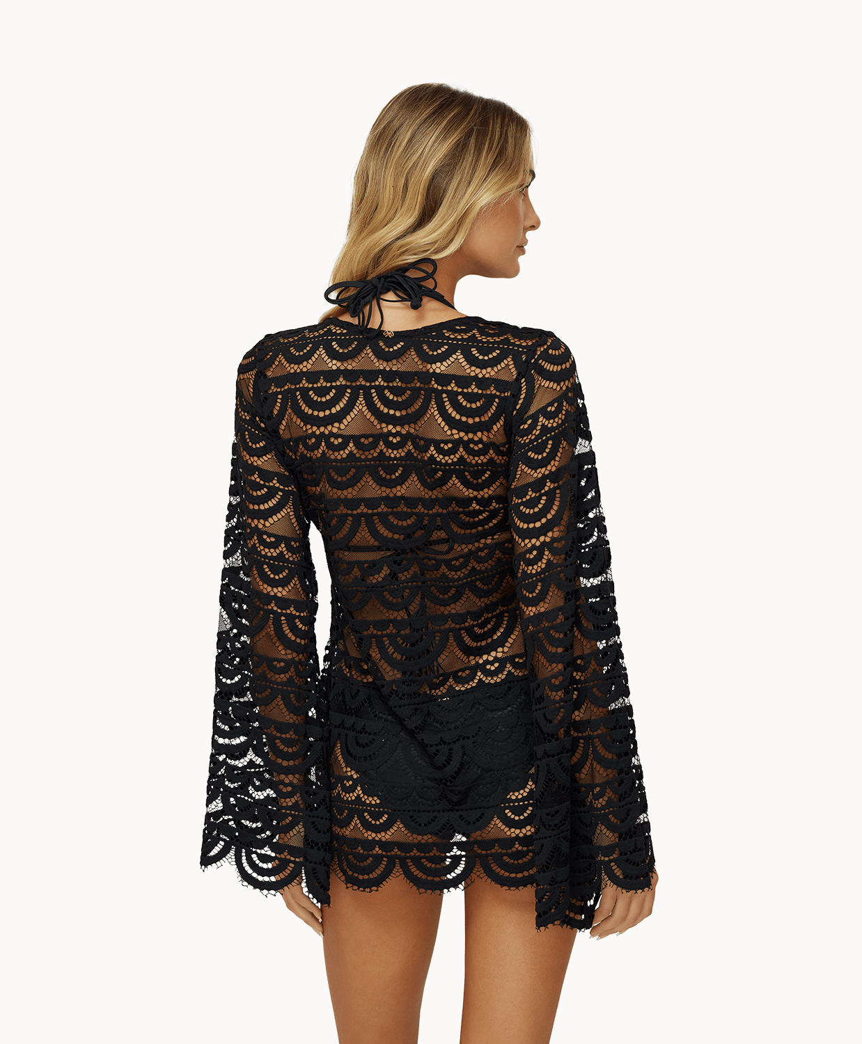 Back view of woman wearing black lace tunic in front of a white background. 