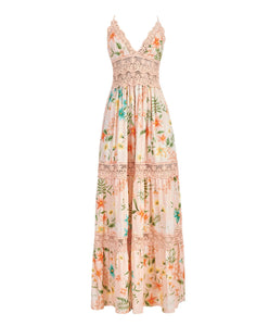 A floor length dress with a tropical print against a white wall. 