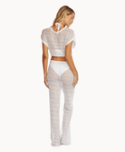 Back view of a woman wearing a matching cream knit top and pants in front of a white background. 