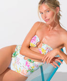 A woman wearing a light blue floral one piece swimsuit sitting on a blue chair. 