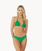 Blonde woman wearing green Isla macrame bikini standing in front of white wall.