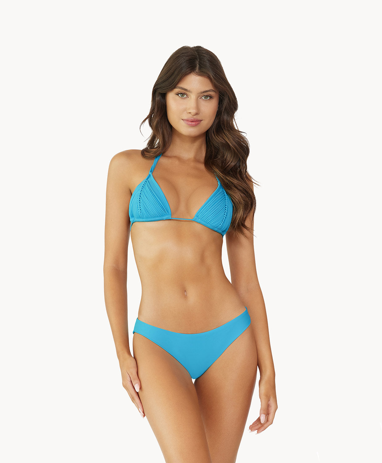 Brunette wearing a turquoise blue bikini stands in front of white wall.