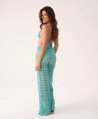 woman wearing a blue lace pant and blue bikini top stands in front of white background