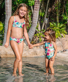 Kids Solana Junie Cut Out One Piece swimsuit with vibrant blue tropical floral print, lettuce-edge trim, and playful cutout details.