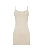 A woman wearing a nude slip dress standing against a white wall.