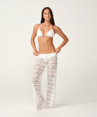 Woman wearing a white bikini and lace pants on a plain background