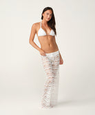 Woman wearing a white bikini and lace pants on a plain background