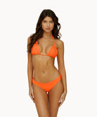 A woman wearing an orange bikini standing against a white wall.