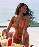 A woman wearing an orange bikini standing near a table outside.