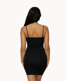 Back view of woman wearing black slip dress in front of a white background. 