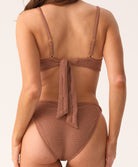 Woman wearing brown bikini set facing white background.