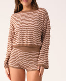 A woman wearing a long sleeve brown and beige striped top and matching shorts standing in front of a white background.