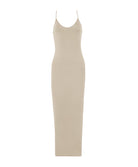 A woman wearing a long nude slip dress facing towards a white wall.