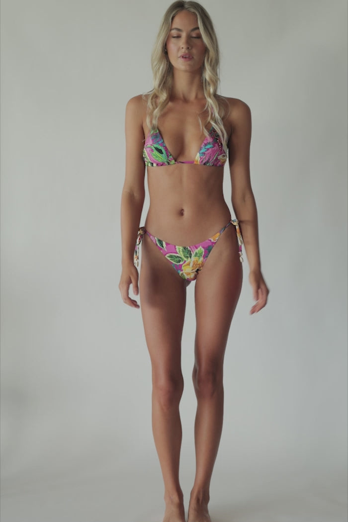 Blonde woman wearing a pink tropical triangle shape bikini with hand-sewn beading spinning around in front of a white wall.