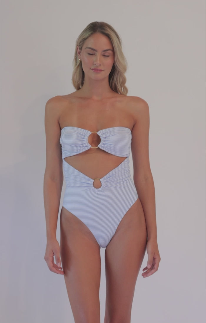 Blonde woman wearing a white strapless one piece spinning in front of a white background. 