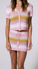 A woman wearing a pink striped crochet shirt and matching skirt spinning in front of a wall. 