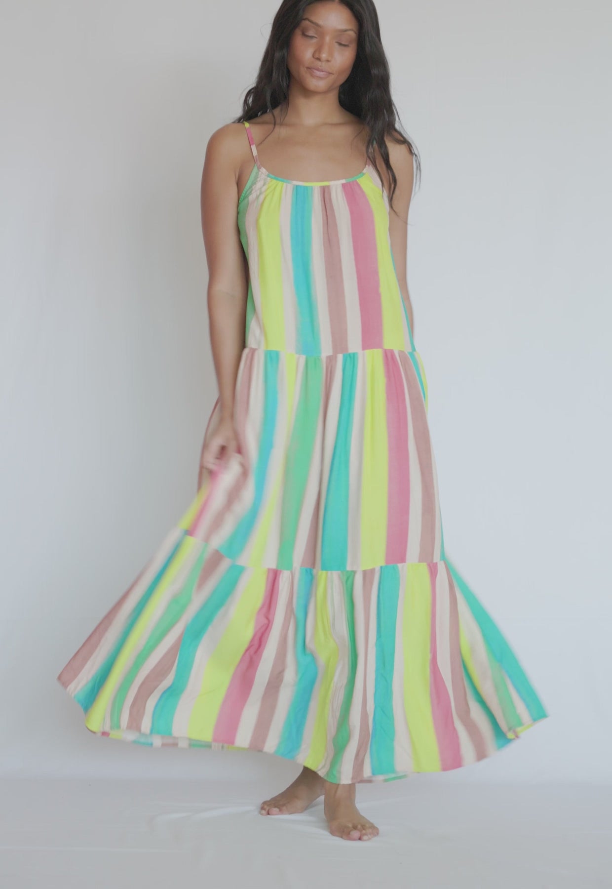 A woman wearing a colorful floor length dress spinning in front of a white wall. 