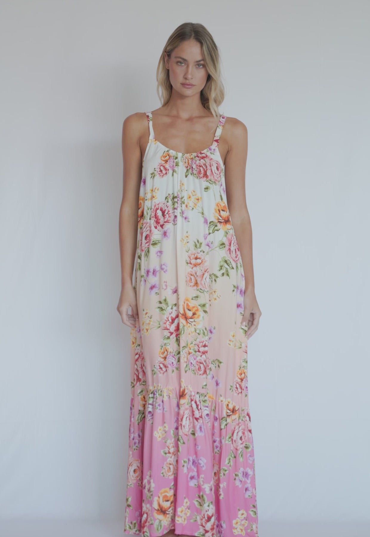 A woman wearing a floor length floral dress spinning in front of a white wall. 