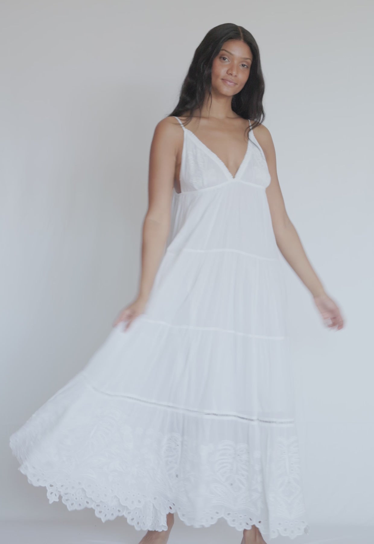 A woman wearing a long white dress spinning in front of a white wall.