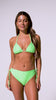 A woman wearing a green triangle top and matching high waist bottoms spinning in front of a white wall.