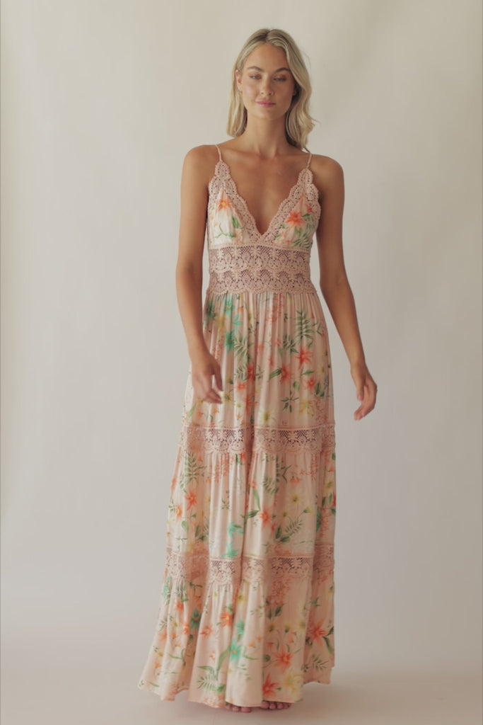 A blonde woman wearing a floor length dress with a tropical print spinning in  front of a white wall.