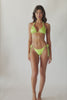 Brunette woman wearing a lime macrame triangle shape bikini spinning around in front of a white wall.