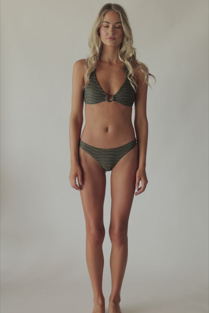 Blonde woman wearing a gray print halter bikini with ring detail spinning around in front of a white wall.