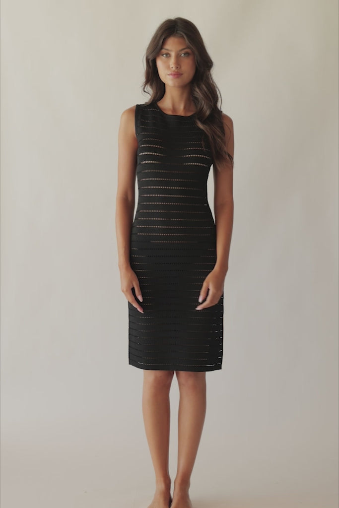 Brunette woman wearing a black short coverup dress with stitching details and side slit spinning around in front of a white wall.