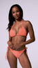 A woman wearing an orange triangle bikini and matching high wait tie side bottoms spinning in front of a white wall.