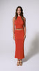A woman wearing a red crochet top and matching long skirt spinning in front of a white wall.