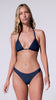 A woman wearing a navy triangle top bikini spinning against a white wall.