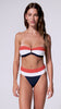 A woman wearing a red, white, and navy bandeau bikini spinning in front of a white wall.
