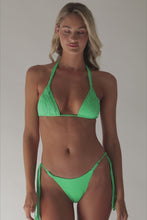 A blonde woman wearing a green bikini spinning in front of a white wall.