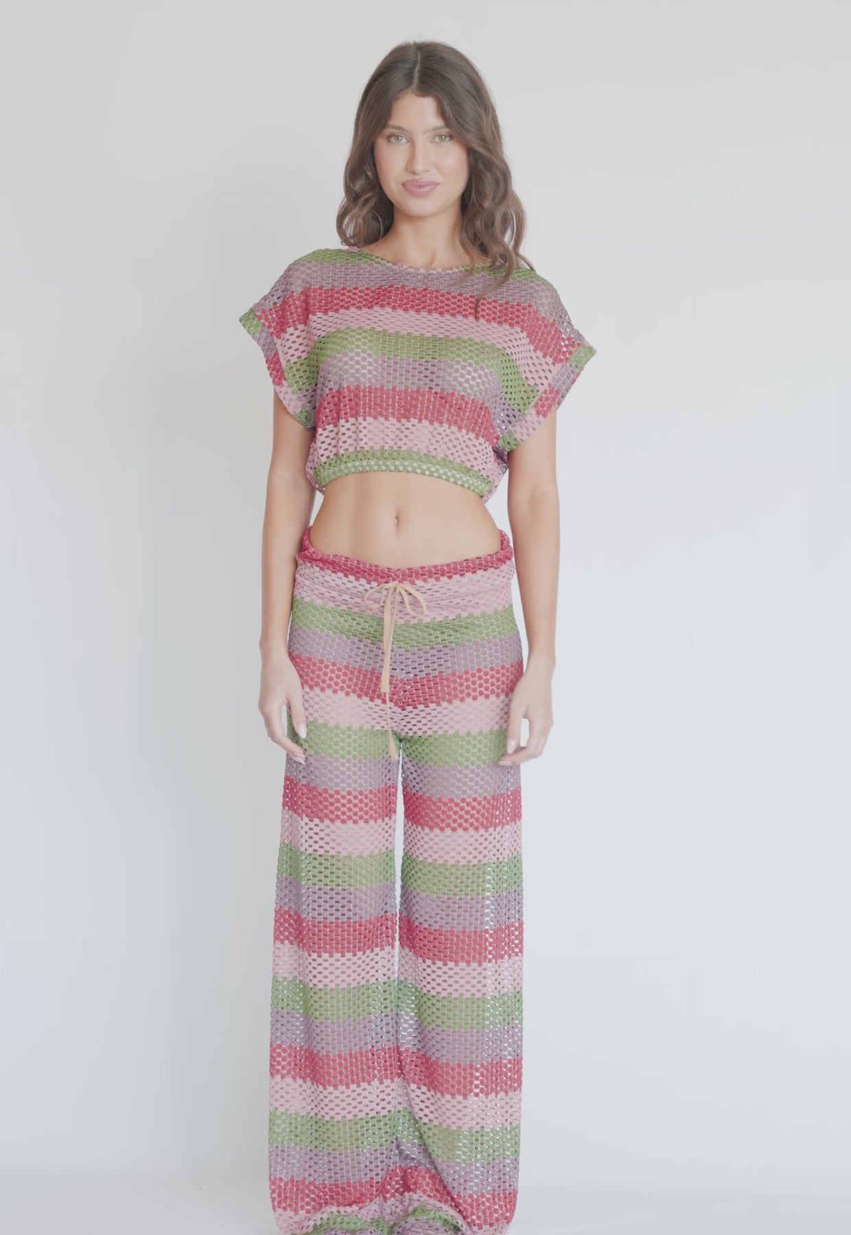 A woman wearing a color block crochet crop top and matching pants spinning in front of a white wall. 