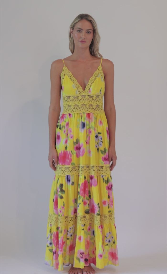 Blonde woman wearing a yellow and flower-patterned flowy dress spinning in front of a white background. 