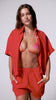 A woman wearing a red and pink bikini top, red short sleeve linen top, and matching linen shorts spinning in front of a white wall. 