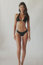 Brunette woman wearing a black bikini spinning in front of a white wall. 
