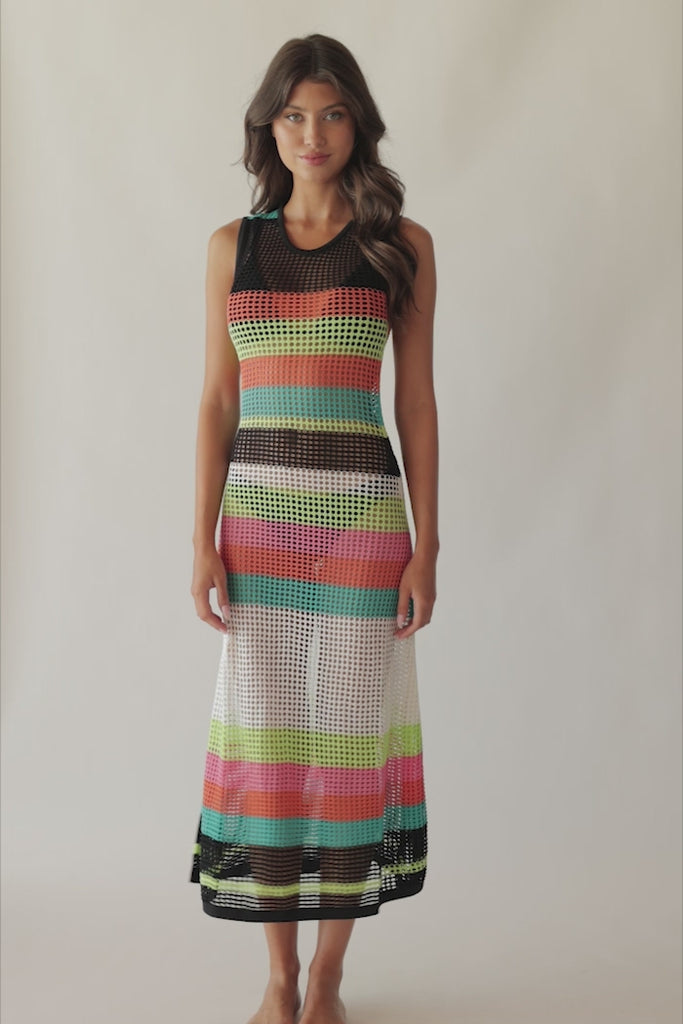 Brunette woman wearing a multi-colored striped full length dress spinning around in front of a white wall.