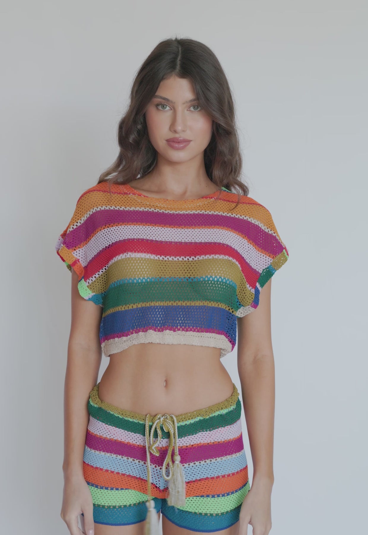 A brunette woman wearing a striped crop top and shorts spinning in front of a white wall. 